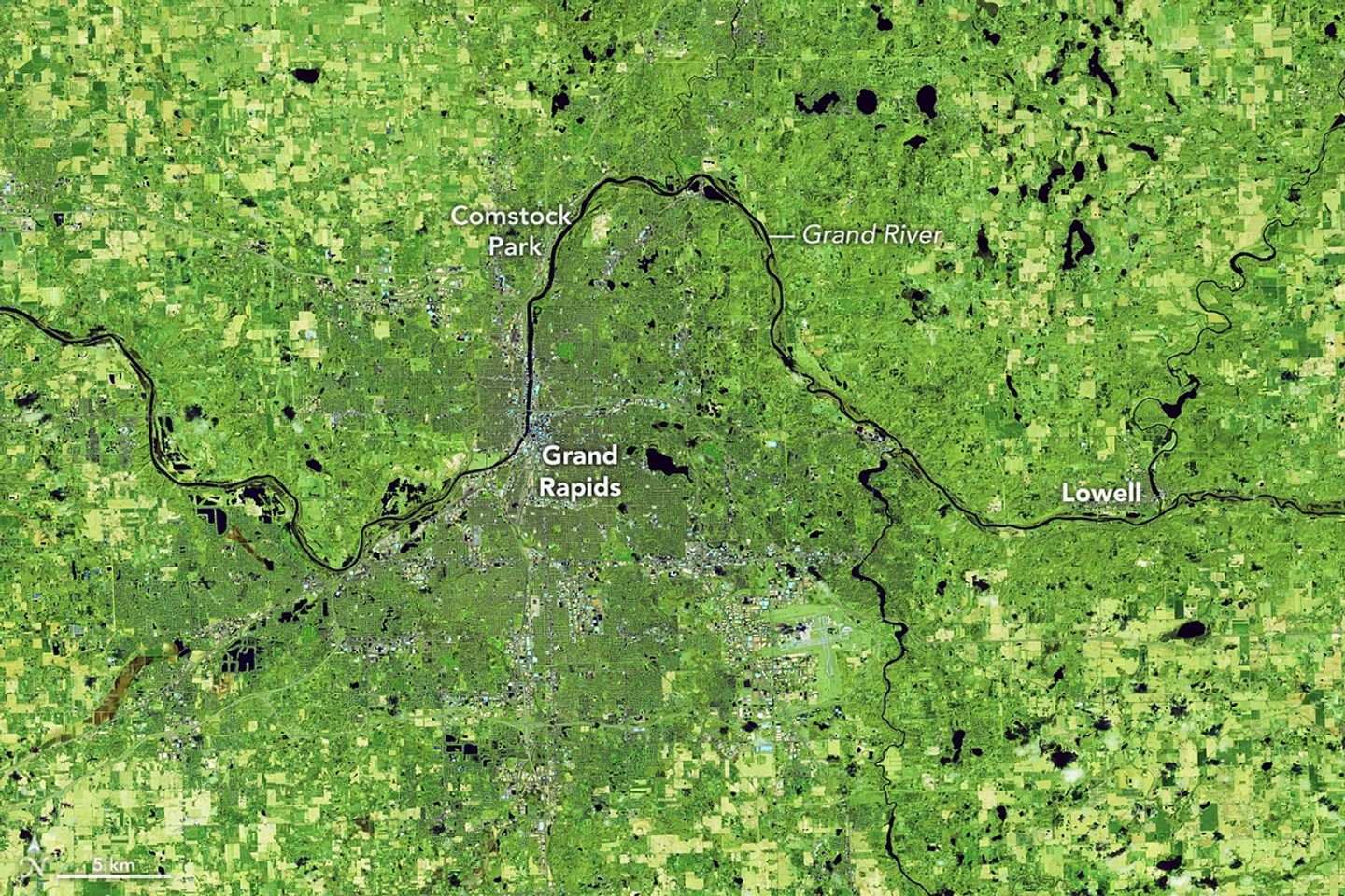 The Grand River in Michigan winds across a false-color image from east to west. Water is dark blue, and vegetation appears in shades of green.